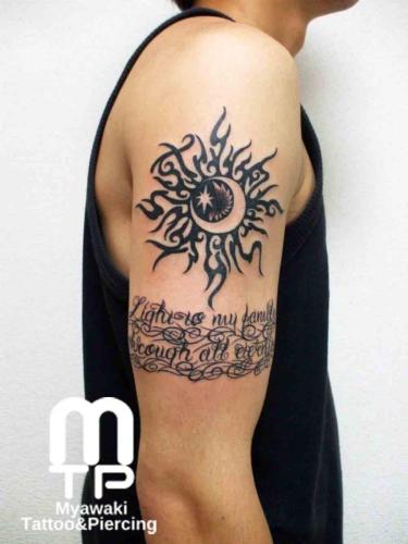 二の腕に太陽・月をイメージしたトライバル風のカスタムデザイン。下にはカスタムレターと装飾