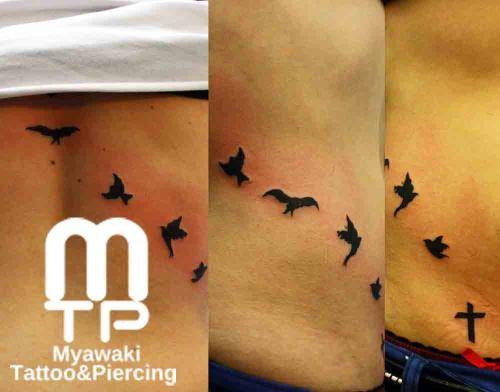 右腰骨～背中にかけて羽ばたく数羽のシルエットでの鳥。腰骨には黒色でシンプルな十字架。