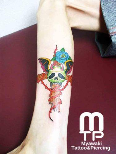ふくらはぎ外側にカラーで赤いイバラの絡んだ十字架が刺さったドクロ、悪魔の羽根、青い薔薇