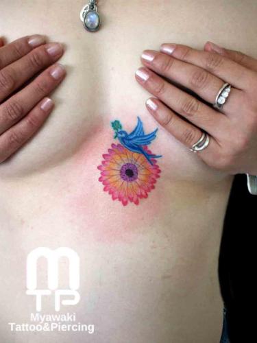 左乳房下にクローバーを咥えた青い鳥と花。