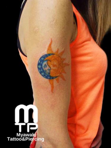 二の腕に青系の三日月、オレンジ系の太陽のツーフェイス。