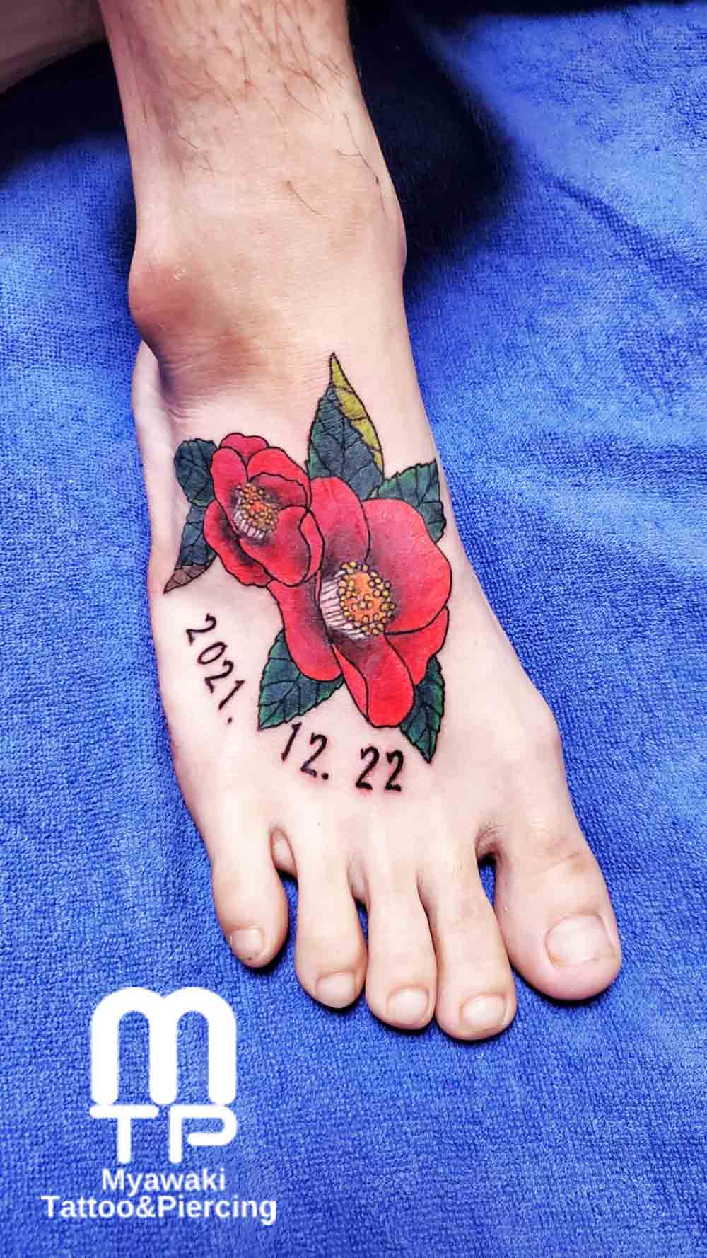 足の甲に赤いリアルな雰囲気の椿のデザインのタトゥー